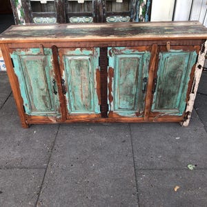 May include: A rectangular wooden sideboard featuring a natural brown wood top and four cabinet doors. The doors are painted in a distressed teal finish with visible wood grain and dark metal hardware, showcasing a weathered and rustic appearance.