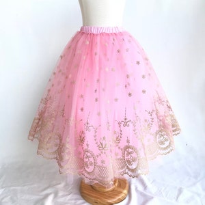 May include: A pink tulle skirt with gold embroidery and a scalloped lace trim. The skirt is on a white mannequin.