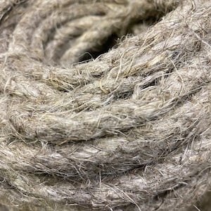 May include: Close-up of a thick, natural fibre rope, showing the individual strands and the braided texture. The rope is a light brown colour.