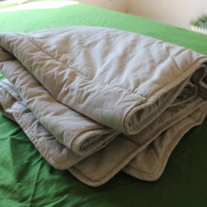 Könnte beinhalten: Eine gefaltete graue Gewichtsdecke mit gestepptem Muster. Die Decke liegt auf einer grünen Oberfläche.