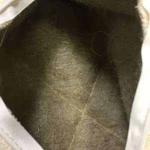 May include: The inside of a white canvas bag with a beige felt lining. The lining has a few loose threads.