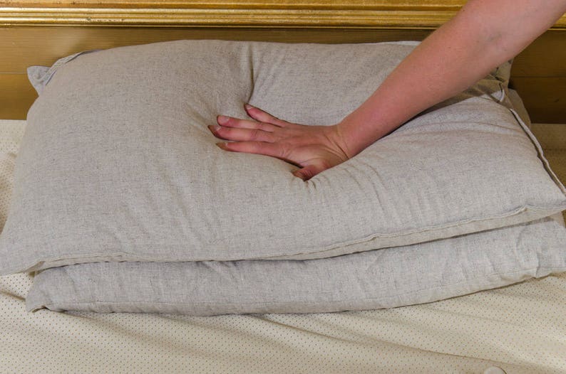 Puede incluir: Primer plano de una mano presionando una almohada gris claro. La almohada est&aacute; hecha de una tela suave y texturizada y est&aacute; colocada sobre otra almohada similar.