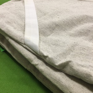 Peut inclure: Un tissu de lin beige plié en plusieurs couches avec un élastique blanc.