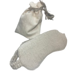 K&ouml;nnte beinhalten: Eine beige Augenmaske aus Leinen mit einem elastischen Band und einem passenden Kordelzugbeutel. Die Maske ist oval geformt und soll das Licht blockieren. Die Tasche ist klein und aus dem gleichen Leinenmaterial gefertigt. Das Set ist ideal zum Entspannen und Schlafen.