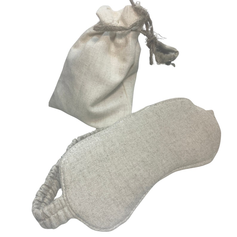 K&ouml;nnte beinhalten: Eine beige Augenmaske aus Leinen mit einem elastischen Band und einem passenden Kordelzugbeutel. Die Maske ist oval geformt und soll das Licht blockieren. Die Tasche ist klein und aus dem gleichen Leinenmaterial gefertigt. Das Set ist ideal zum Entspannen und Schlafen.