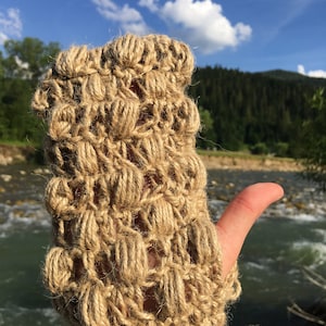May include: A close-up of a beige crocheted fingerless glove with a textured design. The glove is made of natural fibers and has a unique, handmade look.