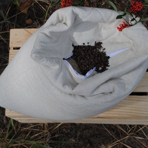 May include: A white linen pillowcase filled with buckwheat hulls. The pillowcase is open and the buckwheat hulls are visible. The pillowcase is sitting on a wooden crate.