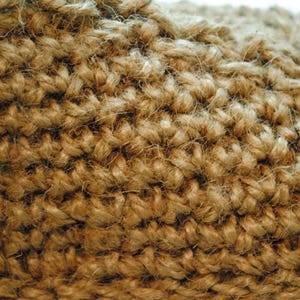 May include: Close-up of a woven jute fabric, showcasing a textured surface. The natural fibers are tightly interlaced, creating a dense, durable material. The color is a warm, earthy brown, suggesting a rustic or natural aesthetic.