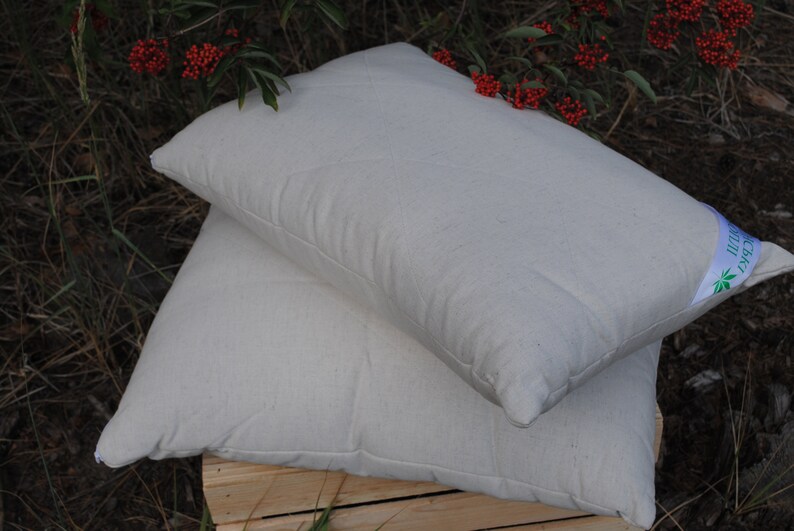 Puede incluir: Dos almohadas blancas de algod&oacute;n org&aacute;nico apiladas una encima de la otra. La almohada superior tiene una etiqueta verde y blanca que dice "Algod&oacute;n org&aacute;nico".