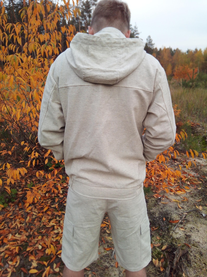 May include: A beige hooded jacket and matching shorts made of linen. The jacket has a zip closure and a drawstring hood. The shorts have two pockets on the sides.