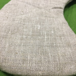 May include: A close-up of a beige linen pillow with a curved shape. The pillow is made of a natural fabric with a woven texture.
