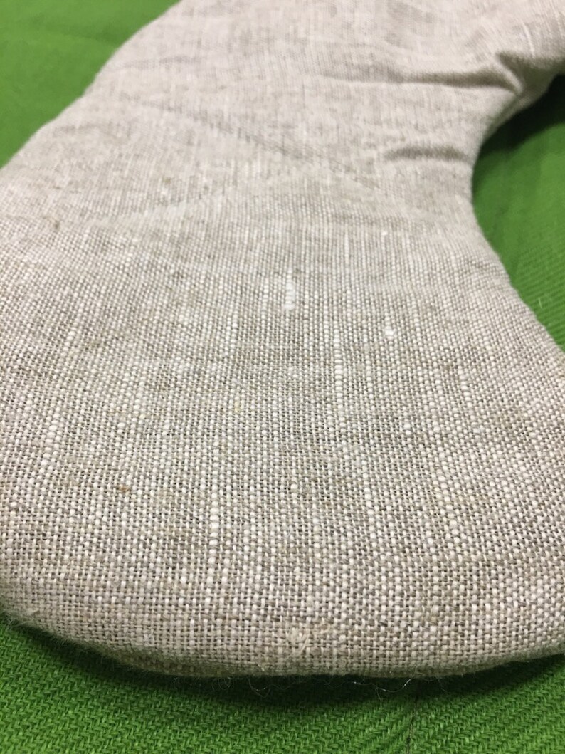 May include: A close-up of a beige linen pillow with a curved shape. The pillow is made of a natural fabric with a woven texture.