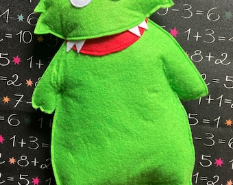 May include: A green felt monster with a big toothy grin and white eyes. The monster is sitting on a black background with white numbers and stars.