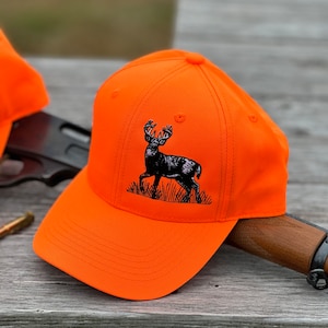 May include: An orange baseball cap with a black embroidered deer silhouette. The cap has a curved brim and a mesh back.