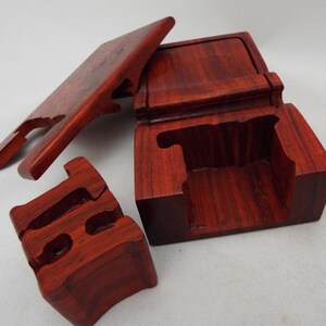 May include: A wooden puzzle box with a red mahogany finish. The box is disassembled, showing the intricate design of the puzzle.
