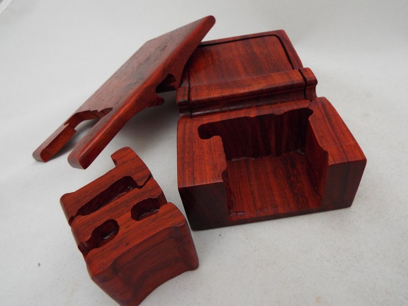 May include: A wooden puzzle box with a red mahogany finish. The box is disassembled, showing the intricate design of the puzzle.