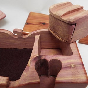 May include: A wooden jewelry box with a hinged lid and a small, separate compartment. The box is made of cedar wood and has a natural reddish-brown color. The interior of the box is lined with a dark brown fabric.
