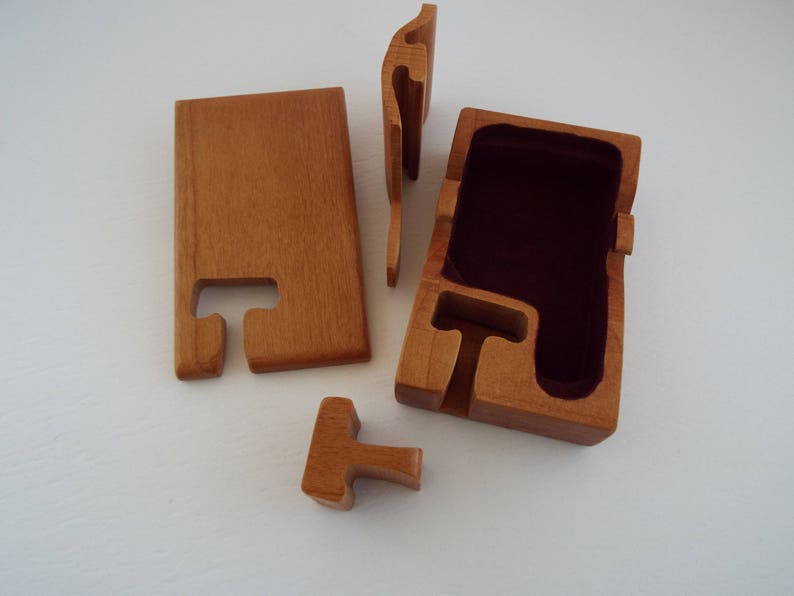 May include: A wooden puzzle box with a red velvet interior. The box is made of five pieces that fit together to create a secure container.