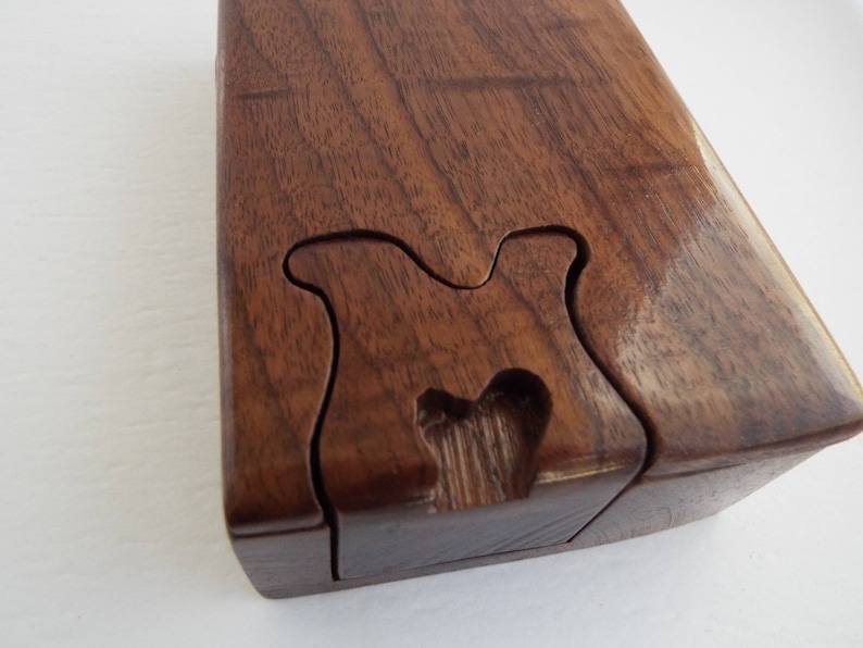 May include: A wooden puzzle box with a unique, intricate design. The box is made of dark brown wood and has a smooth, polished finish.