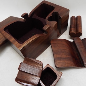 May include: A wooden puzzle box with multiple compartments and a hinged lid. The box is made of dark brown wood and has a smooth finish. The box is open and the compartments are visible.