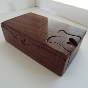 May include: A dark brown wooden puzzle box with intricate cutouts. The box is closed and has a smooth, polished finish.