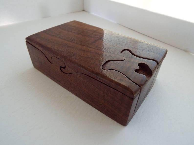 May include: A dark brown wooden puzzle box with intricate cutouts. The box is closed and has a smooth, polished finish.