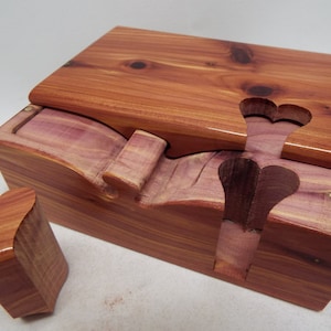 May include: A wooden box with a heart-shaped opening and a separate heart-shaped piece. The box is made of cedar wood and has a natural reddish-brown color.