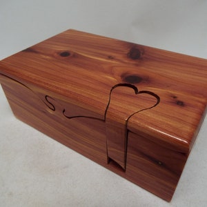 May include: A wooden box with a heart-shaped cutout and the letter "S" carved into the lid. The box is made of cedar wood and has a natural reddish-brown color.