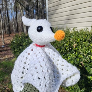 May include: A handmade crochet Zero plush toy from The Nightmare Before Christmas. The white plush features black eyes, an orange nose, and a red collar. The plush is wearing a white blanket.