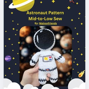 May include: A crocheted astronaut doll in a white spacesuit with black accents, held against a space-themed background. The image includes text that reads "Astronaut Pattern Mid-to-Low Sew By: Mainsnfriends."