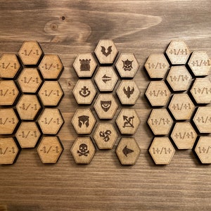 May include: A set of wooden game pieces with various symbols and numbers. The pieces are hexagonal and have a light brown color. The symbols include a skull, a castle, a bat, an arrow, and a ship. The numbers include -1/-1, +1/+1, and 1+/14.
