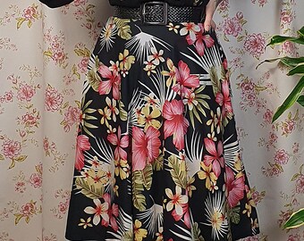 May include: A vintage-inspired outfit featuring a black floral skirt with pink and yellow flowers, a sheer black blouse with small yellow floral accents, and a black belt. The ensemble is completed with a red beret and black shoes.