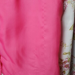 May include: A bright pink short-sleeved blouse with a smooth, silky texture. The blouse is folded and displayed on a white background with a floral pattern.