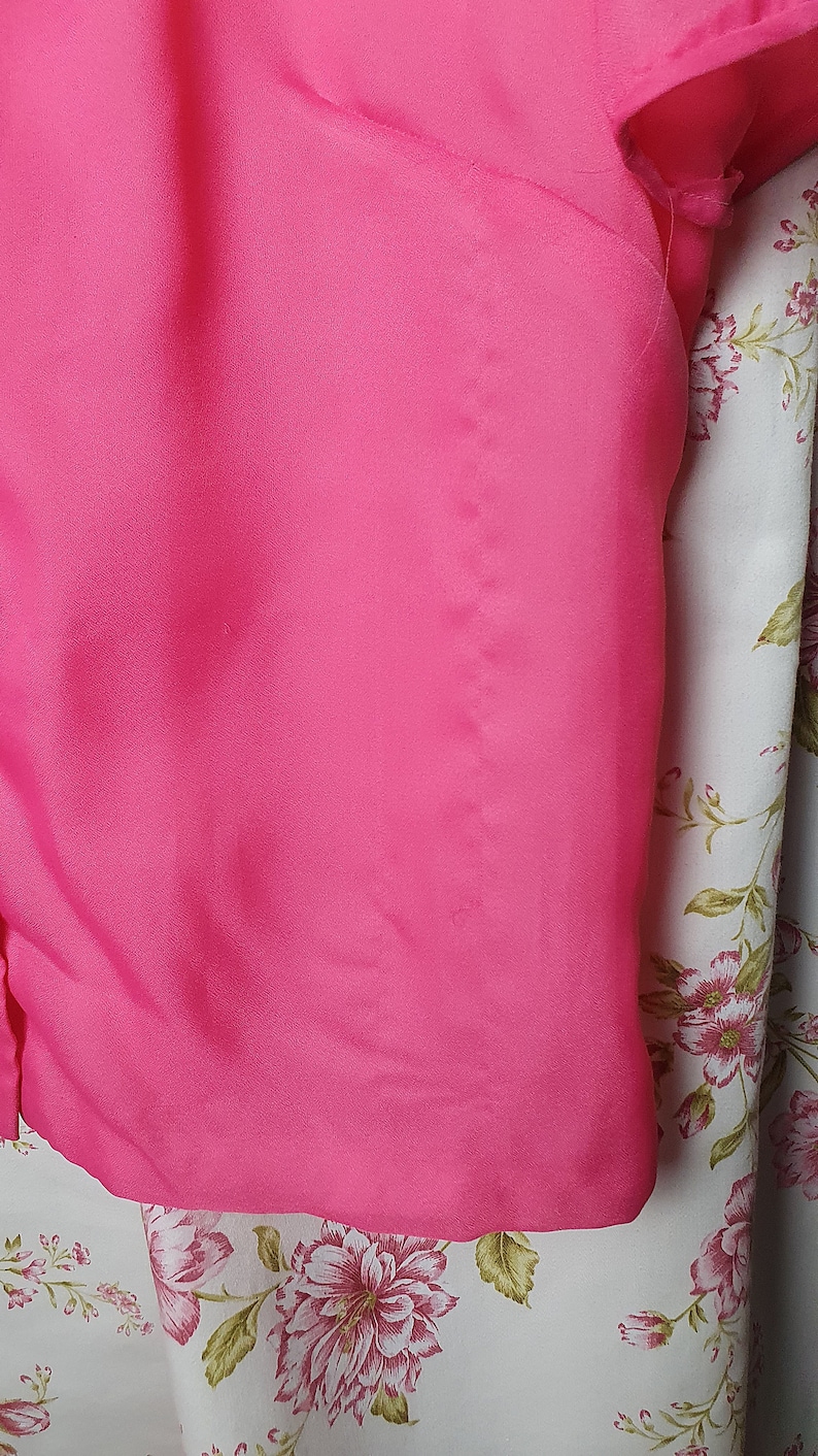 May include: A bright pink short-sleeved blouse with a smooth, silky texture. The blouse is folded and displayed on a white background with a floral pattern.