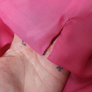 May include: A close-up of a pink fabric with a small tear. The fabric is held in a hand.