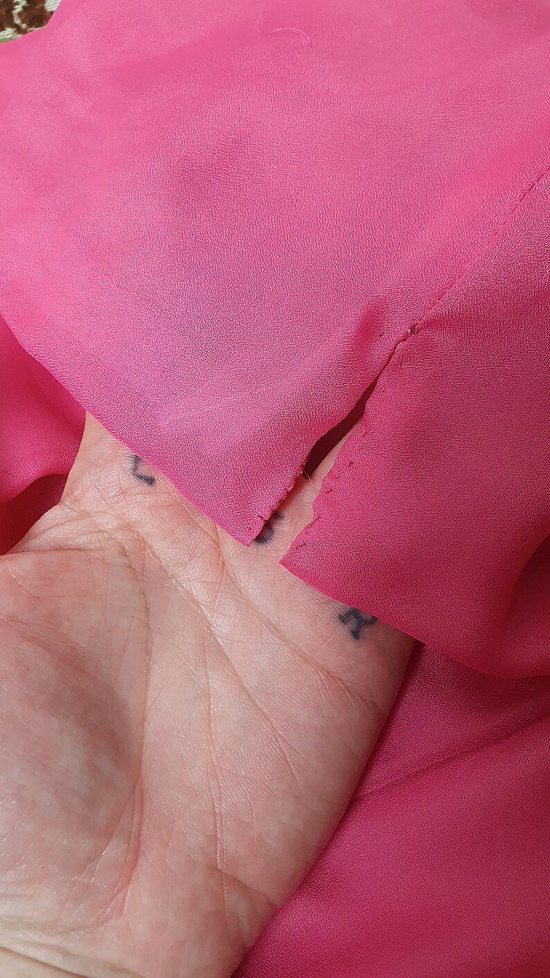 May include: A close-up of a pink fabric with a small tear. The fabric is held in a hand.