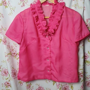 May include: A pink short-sleeved blouse with a ruffled collar and button closure.