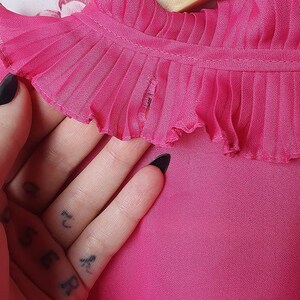 May include: A pink blouse with a ruffled collar. The collar has a small tear in the fabric.