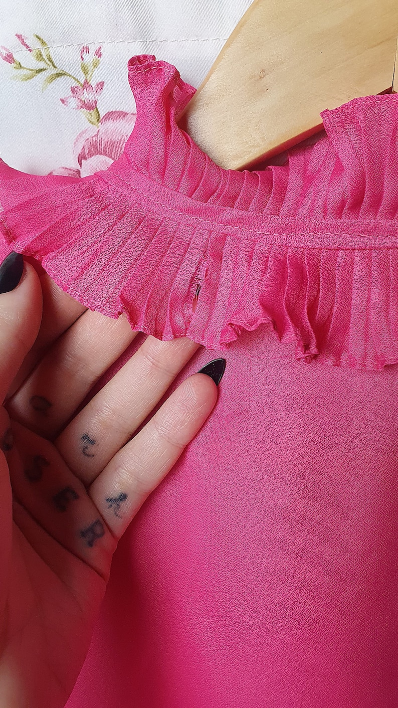May include: A pink blouse with a ruffled collar. The collar has a small tear in the fabric.