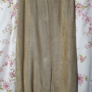May include: A brown suede skirt with a straight silhouette and a center front slit. The skirt has a waistband with a button closure.