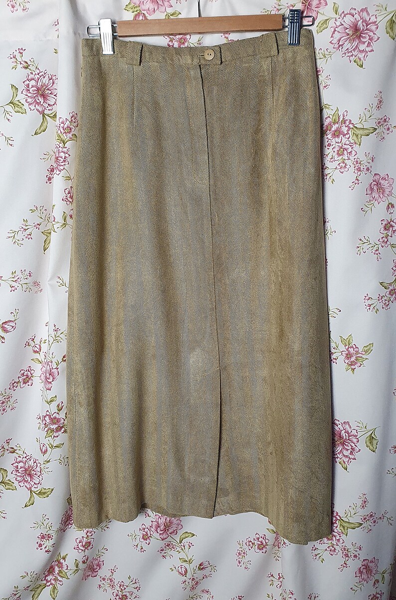 May include: A brown suede skirt with a straight silhouette and a center front slit. The skirt has a waistband with a button closure.