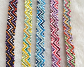 May include: Five handmade woven friendship bracelets featuring a repeating chevron pattern. The bracelets display various color combinations including black, orange, and purple; yellow, green, and white; light and dark blue; pink, red, and white; and multicolored pastel threads.