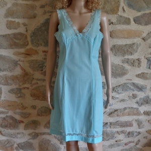 Può includere: Un sottoveste azzurra con scollo a V e finiture in pizzo. L'abito senza maniche presenta un corpetto aderente e una gonna dritta, con dettagli in pizzo lungo lo scollo e l'orlo. L'abito è esposto su un manichino.