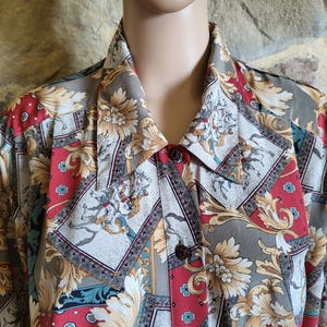 Può includere: Camicia abbottonata con un motivo ripetuto di motivi floreali ed equestri in rosso, grigio e oro. La camicia ha un colletto classico e bottoni marrone scuro. Il tessuto sembra essere leggero.