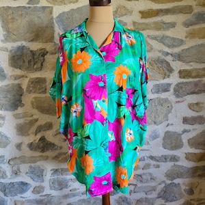 May include: A vibrant, short-sleeved shirt with a colorful floral pattern. The shirt features a teal background with large orange and pink flowers, and green leaves. The shirt is buttoned and displayed on a mannequin.