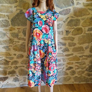 May include: A colorful floral print dress with a scoop neckline and short sleeves. The dress features a vibrant pattern of red, yellow, blue, and purple flowers on a black background. The dress is knee-length and has a relaxed fit.