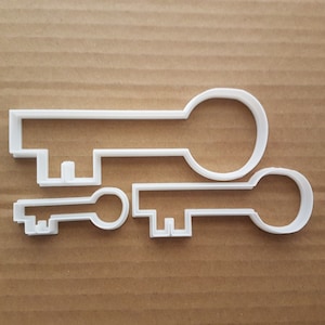 May include: Two white plastic cookie cutters shaped like keys. The larger key is about 10 cm long and the smaller key is about 5 cm long.
