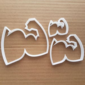 Può includere: Set di quattro tagliabiscotti in plastica bianca a forma di bicipiti. I tagliabiscotti sono progettati per realizzare biscotti o decorazioni di pasta di zucchero.