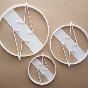 May include: Three white plastic cookie cutters in the shape of a lightning bolt inside a circle. The cutters are different sizes.