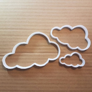 May include: Three white plastic cookie cutters shaped like clouds. The largest cloud is in the center, with a smaller cloud to the right and a very small cloud to the bottom right.